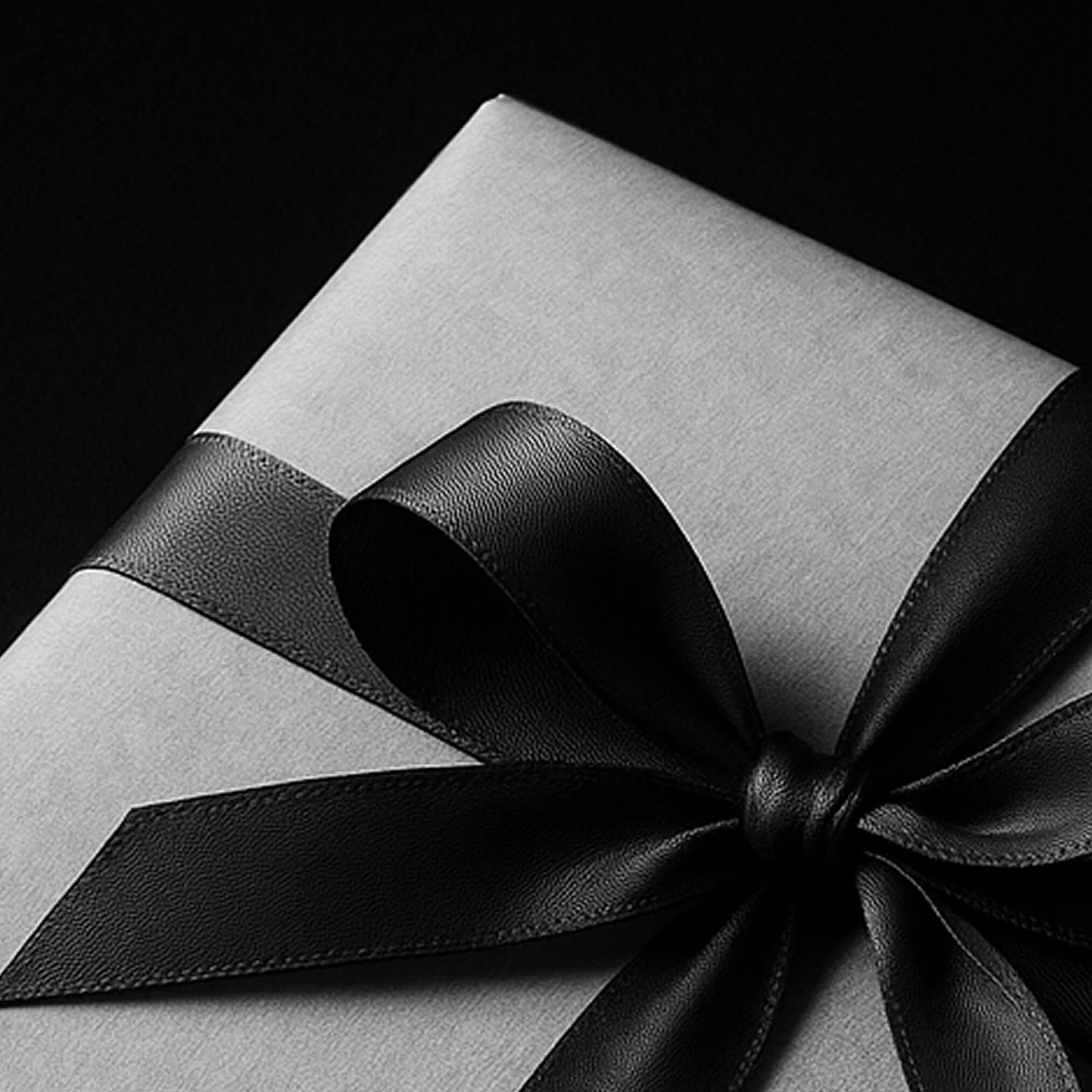 Edle Geschenkbox mit schwarzem Band und Schleife auf dunklem Hintergrund – stilvolles Präsent für besondere Anlässe.